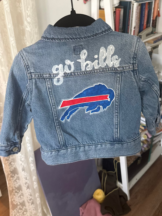 Denim jacket with 'go bills' text and logo on a hanger in a room.
